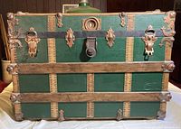 Front view of large green steamer trunk with wood slats, metal rivets, and keyed lock.
