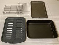 Full set of metal ovenware items: roasting pan, baking sheet, 2-piece broiler pan, and 2 cooling racks arranged on table.