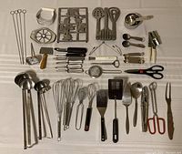 Image of an assortment of kitchen tools including ladles, whisks, measuring scoops and spoons, and other kitchen utensils displayed on a flat surface.