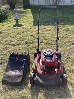 Photo of the red Craftsman gas push lawn mower positioned on grass with the black leaf bag placed beside it.