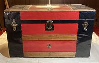 Front view of red and black wooden steamer trunk with metal clasps and latch, showing its design and condition.