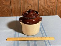 Full view of Robinson Ransbottom Pottery covered pot with lid on a table and wood background, with a ruler in front for scale.
