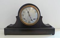 Front view of Sessions mantel clock showing curved wooden case, glass protected dial with Arabic numerals and black hands, brass bezel.