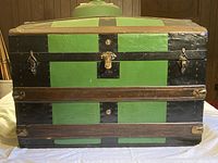 Front exterior view of the small steamer trunk showing green and black painted panels, wood reinforcements, and metal locks.