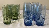 Photo showing 4 green and 4 blue textured drinking glasses in a row on a white surface.