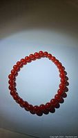 Top view of stretchy bracelet made of round, polished red carnelian beads arranged in a circle on a white background.