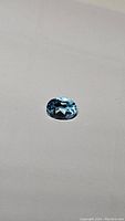 Close-up image of an oval cut blue gemstone, showing facets and gleaming luster on a plain background.