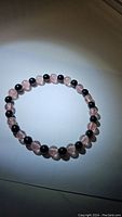 Clear photo of a stretchy gemstone bracelet made with alternating natural jet black onyx beads and pinkish translucent strawberry quartz beads.