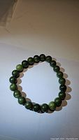 Front view of green jade natural bead stretchy bracelet on white surface.