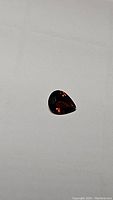 Pear cut deep burnt orange tourmaline gemstone on white background showing its size and color in natural light.