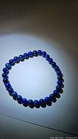 Photo showing entire Lapis Lazuli bead bracelet arranged in a circular shape under spotlight, highlighting deep blue color.