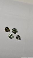 Four mixed colored round faceted sapphires on white background showing different hues: yellow, green, light green, and very light blue.