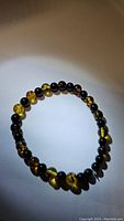 Bracelet laid out in loose circular shape on a plain light surface, showing the alternating amber and black onyx beads under soft lighting.