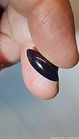 Close-up image of natural Ethiopian black opal held between fingers showing marquis cabochon cut and dark body color with light reflections.