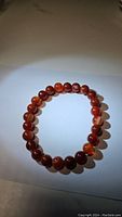 Top view of natural red agate bracelet on white surface showing round, polished beads with visible natural banding and color variation.