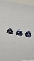 Front view of three natural tanzanite trillion cut gemstones with blue and purple hues arranged on a white background.