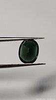 Front view of oval faceted chrome tourmaline held in tweezers against neutral background