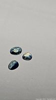 Three natural untreated rose cut sapphires displayed on a neutral background, showing blue, white, and green tones.