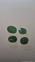 Four natural Zambian emerald gemstones on white surface, showing their size and oval shape under normal light