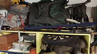 Photo of various fishing backpacks, rods in blue covers, and stacked tackle boxes with a dart board on top.