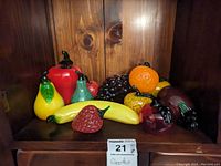 Overall view of glass fruit and vegetable collection on wood shelf.
