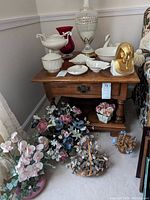 Photo showing several Lenox white bowls, candy dishes, urn and ashtray on wooden table along with a red glass vase and Lenox King Tut mask figurine. Floral arrangements surround the table.