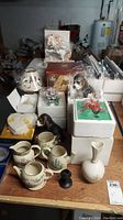 Wide shot showing multiple Lenox items on table including vases, dog figurine, cups, and floral pieces mostly still boxed.