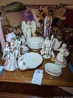 Overall view of Lenox porcelain figurines including Romeo and Juliet, Santa and Mrs. Claus, angel figures, and various trinket dishes displayed on a table.