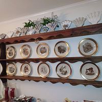 10 Lenox Bohemian Woodland Wildlife plates displayed on wooden rack with detailed animal paintings and gold rims.