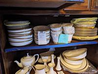 Lenox Eternal pattern place settings stacked on a wooden shelf, including plates, bowls, teapot, gravy boat, and candlestick holders.