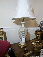 Full view of lamp on side table showing overall shape, lampshade, and bust statue next to it for scale.