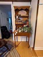 Front view of wooden secretary hutch placed in a corner with various decorative items on top (contents not included)