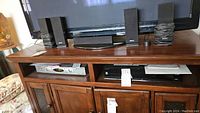 Photo showing six black Sony speakers with cables arranged on a wooden cabinet beneath a TV.