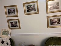 Wide shot showing five framed Thomas Kinkade bridge prints hung on a wall above a green couch.
