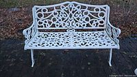 Front view of white wrought iron love seat showing ornate scrollwork and floral patterns, two separate seat sections, and curled armrests.