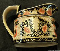 Side view of antique porcelain creamer showing detailed floral and leaf gold-painted design on navy background