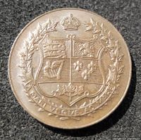 Close-up of the obverse side of the medallion featuring a shield with heraldic elements, a crown above, and a maple leaf wreath surrounding it.