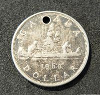 Front side of the 1960 Canadian one dollar silver coin showing canoe design and drilled hole.