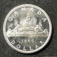 Obverse of the 1965 Canadian silver dollar coin showing the canoe design with two paddlers and trees in the background, along with the year 1965 and inscriptions 'CANADA DOLLAR'.