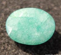 Close-up photo of oval emerald gemstone showing color, cut and surface details