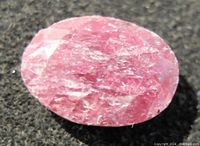 Close-up photo of an oval shaped ruby gemstone showing natural surface imperfections and inclusions.