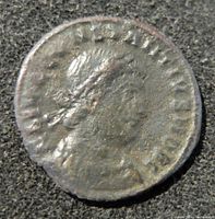 Obverse side of an ancient Roman coin featuring a right-facing laurel or helmeted portrait with surrounding inscriptions, photographed on a textured background.