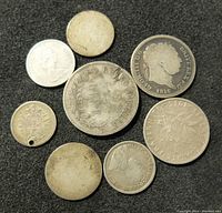 Eight old silver coins arranged on a black surface, showing various inscriptions, portraits, and symbols.
