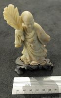 Front view of the stone carved Asian figure holding a fan, showing detailed carving and approximate size with ruler.