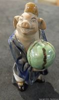 Porcelain pig figurine front view holding green spherical object