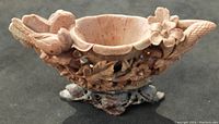 Front angled view of the pinkish stone carved bowl with birds and flower motifs, showing detailed carving and part of the base stand.