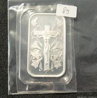 Silver bar featuring Jesus on the cross with lilies and birds in the background, in plastic sleeve.
