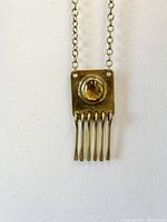 Close-up of pendant showing amber-colored glass cabochon and six brass dangle bars.