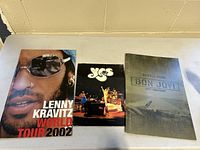 Photo of three classic rock concert tour books arranged side-by-side: Lenny Kravitz World Tour 2002, Yes, Bon Jovi Lost Highway 2007-2008