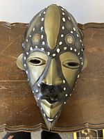 Front view of carved wood mask with bronze accents and embedded coins